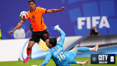 A soccer player from the Netherlands national team wearing jersey number 14 attempts to score against an opposing goalkeeper wearing jersey number 16 at the FIFA City World Cup.