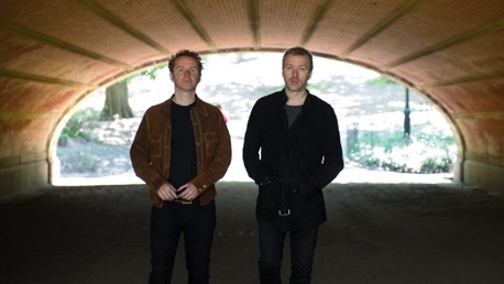 Two individuals standing under a brick tunnel in a park.