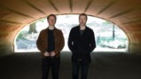 Two individuals standing under a brick tunnel in a park.