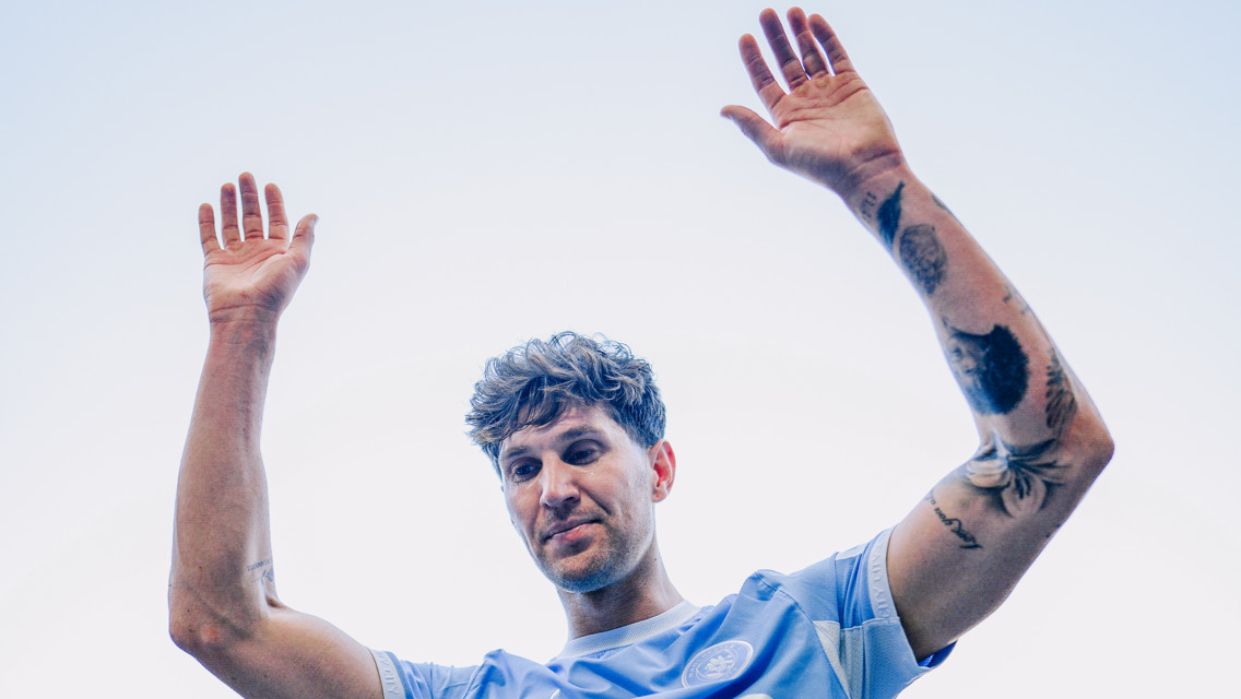 A person wearing a light blue soccer jersey raises their arms, displaying tattoos on both arms.