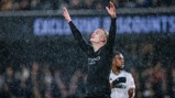 A Manchester City player celebrating in the rain with arms raised, wearing a black kit with visible 'Etihad Airways' logo.