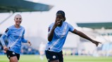 Two Manchester City Women's team players celebrate a goal on the field. One player is pointing forward. They are wearing light blue kits with the Etihad Airways logo.