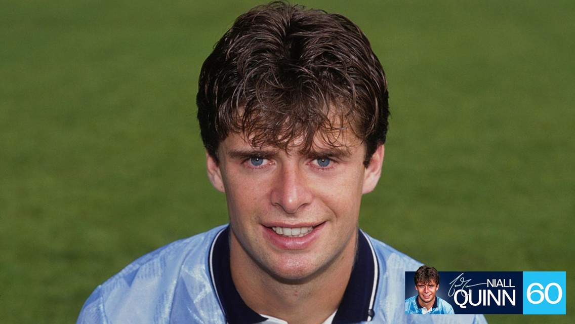 A portrait of a young man with curly hair wearing a light blue football jersey on a green field. There is a watermark with the name 'Niall Quinn' and a number '60'.