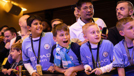 Fans wearing Manchester City jerseys attending an event, some holding phones and scarves.