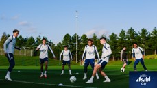 Manchester City players in training on a grassy field wearing Manchester City attire with Asahi Super Dry logo visible.