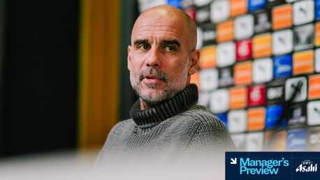 A person in a grey sweater at a press conference with a blurred face. Background features colorful logos and microphones. Text overlay: 'Manager's Preview' and 'Asahi Super Dry'.