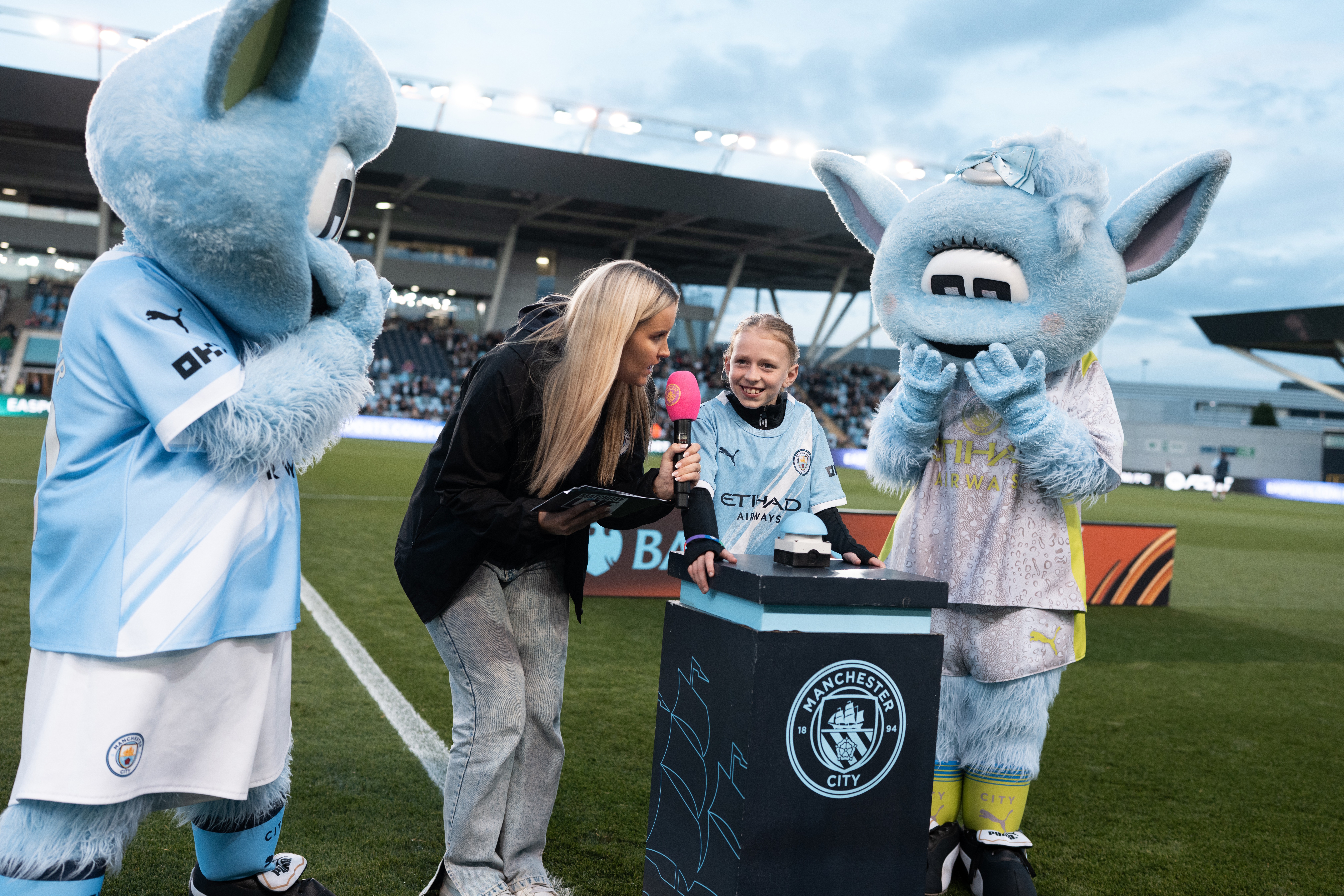 Manchester City mascots Moonbeam and Moonchester interacting with people at a stadium event.