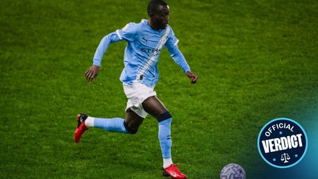 A player in a Manchester City jersey is running on a soccer field, focused on a ball ahead. The Man City crest is visible on the uniform, and there's a logo in the corner with 'Official Verdict.'