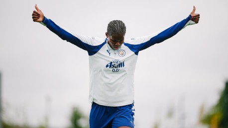 Football player wearing Leicester City training gear stands with arms outstretched, giving thumbs up.