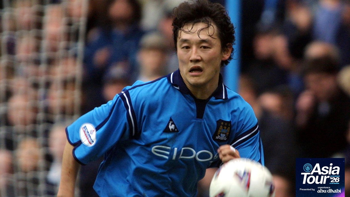 A football player in a Manchester City jersey during a game action shot, wearing a light blue kit and running with the ball. The Asia Tour 2026 logo is visible in the corner.