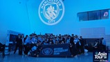 A group photo of Manchester City Official Supporters Club holding a banner at the Asia Tour '26 event. The Manchester City crest is projected on the wall behind them.