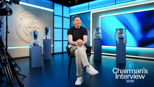 A person seated in a studio with Manchester City branding, surrounded by football trophies. Text reads 'Chairman's Interview 2026'.