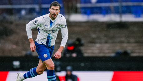 Football player in Manchester City kit running on the field during a match.