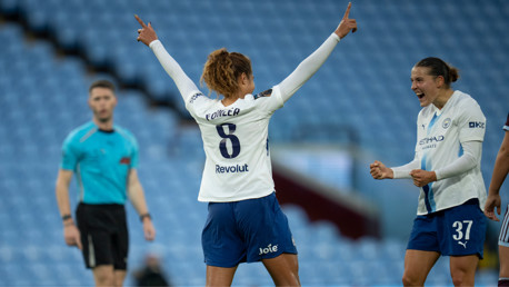 A Manchester City Women's player, wearing number 8 with 'Fowler' on her jersey, celebrates with arms raised alongside a teammate, in a soccer stadium with a referee in the background.