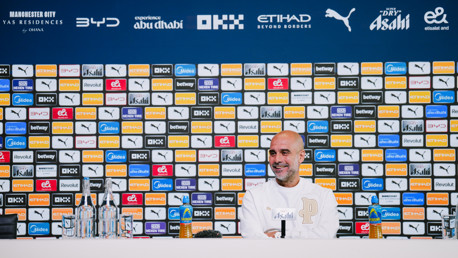 Manchester City press conference with a branded backdrop featuring various sponsor logos.