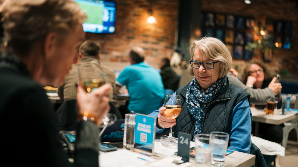 People enjoying drinks at a restaurant with a blurred view of a televised sports game in the background.