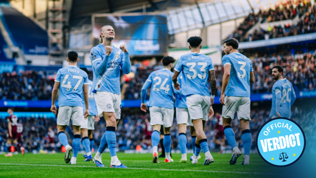 Players from Manchester City celebrate a goal at a football match at Etihad Stadium. Visible players have their names on the jerseys, and fans are in the background.