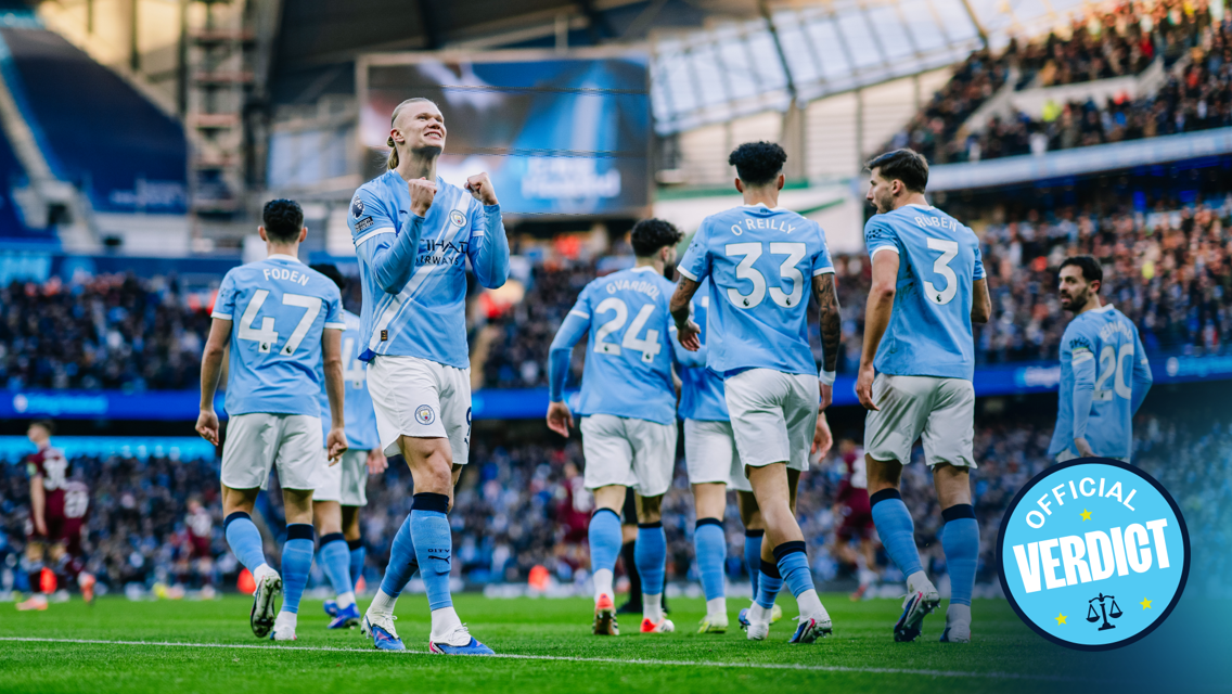 Players from Manchester City celebrate a goal at a football match at Etihad Stadium. Visible players have their names on the jerseys, and fans are in the background.