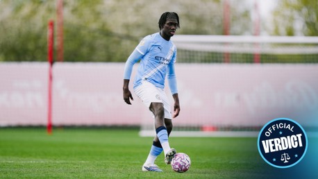 Football player in Manchester City kit during training session holding a ball on the field.