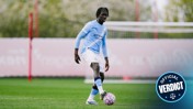 Football player in Manchester City kit during training session holding a ball on the field.