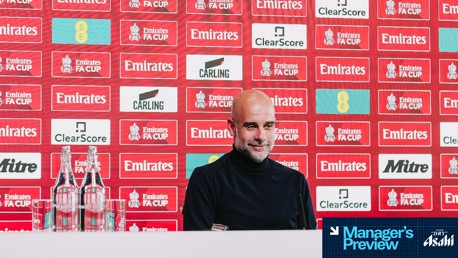A person in a dark sweater is at a press conference in front of a backdrop with FA Cup logos and sponsors like Carling and Clearscore. Bottled water is on the desk, with 'Manager's Preview' text in the corner.