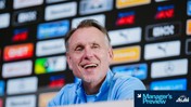 Blurred face of a person in a blue shirt at a press conference with sponsorship logos behind. 'Manager’s Preview' text in the corner.