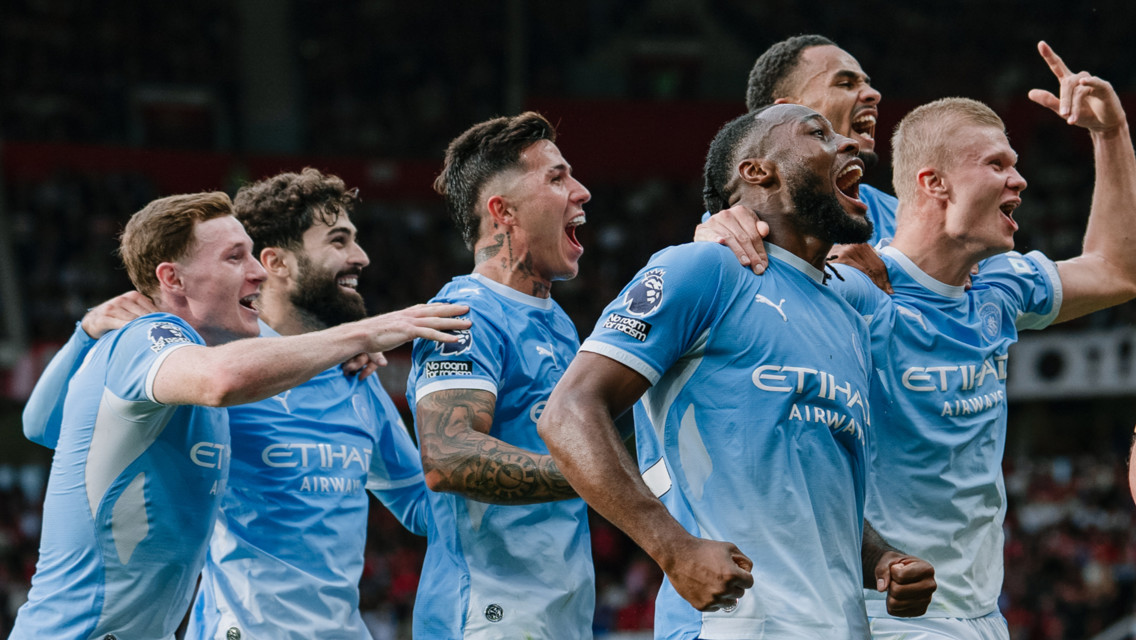 A group of Manchester City players wearing light blue jerseys are celebrating together on the field, displaying expressions of joy and excitement.