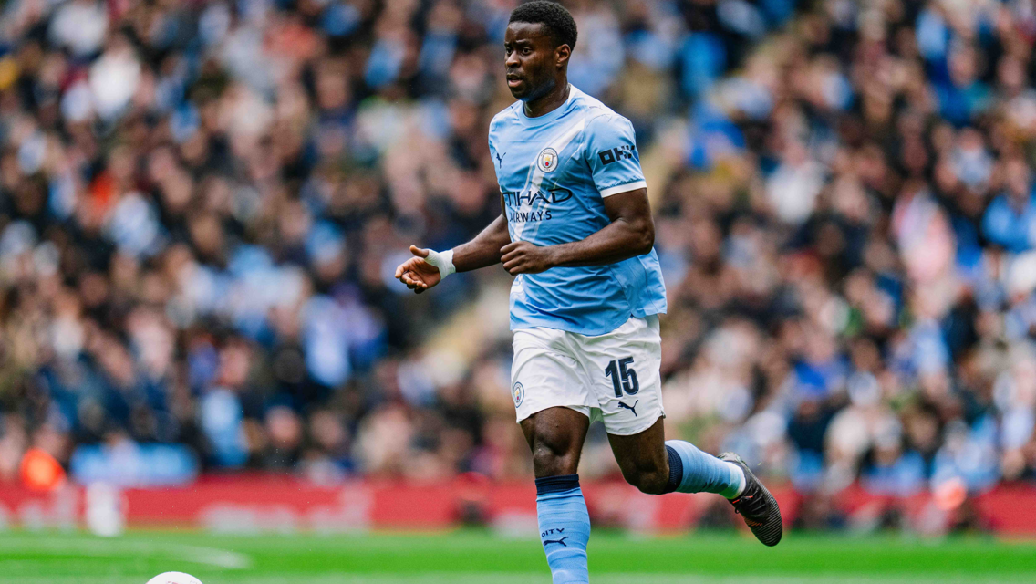 A football player wearing a Manchester City kit with number 15 is running on the field.