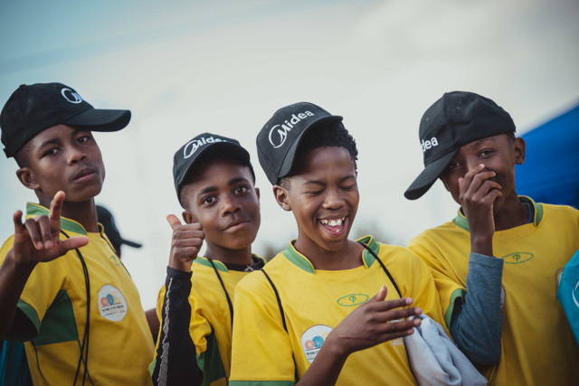 Children wearing yellow shirts and caps, some making hand gestures.