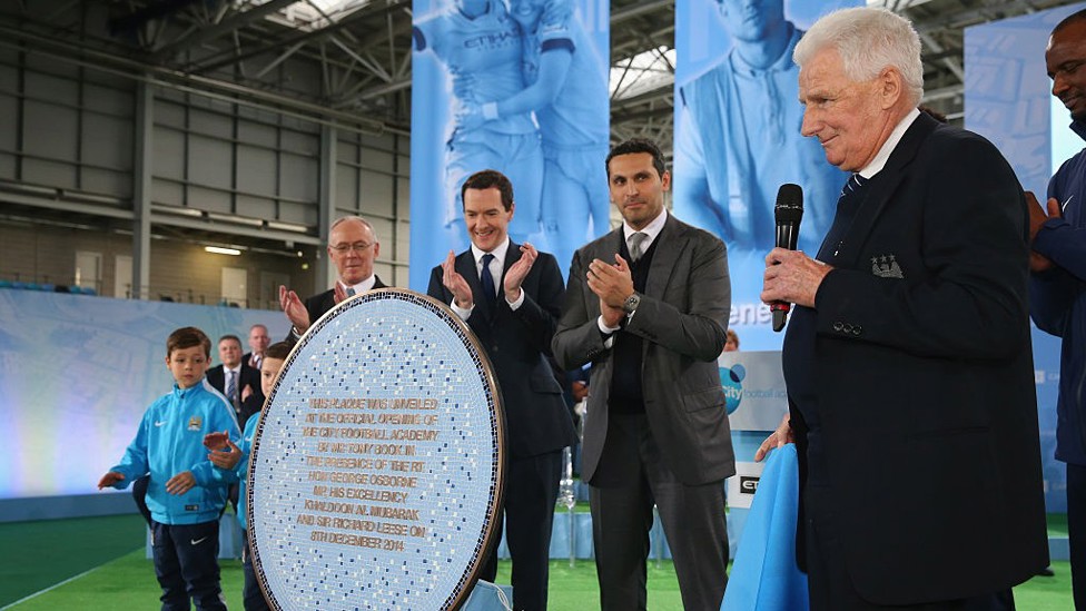 DEEMBRO DE 2014 : A lenda do City, Tony Book, inaugura a City Football Academy, uma instalação de primeira classe para as equipes masculina, feminina e juvenil.