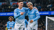 Two Manchester City players in light blue jerseys celebrate a goal during a match, with one player pointing at the other.