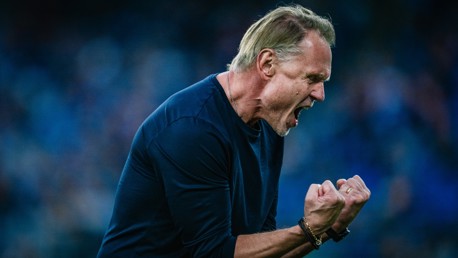 A man in a dark shirt is showing a strong emotional reaction, possibly a celebration or frustration, with fists clenched and mouth open.