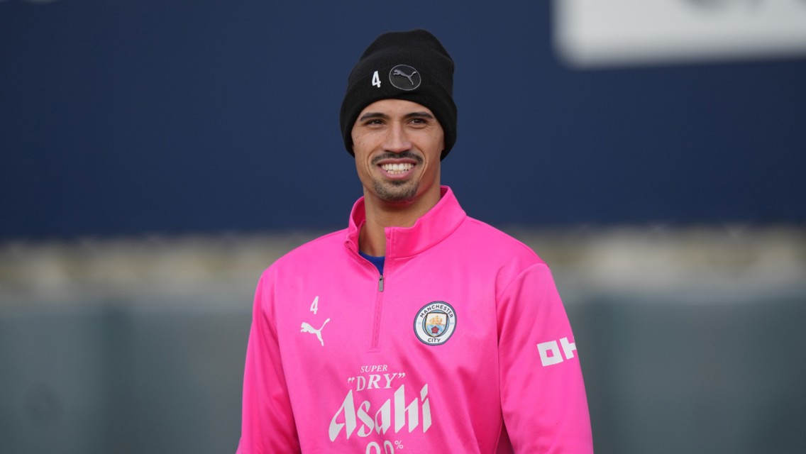 A person wearing a pink Puma training top with Manchester City logo, featuring number 4. The head is covered by a black Puma beanie, blurred face.