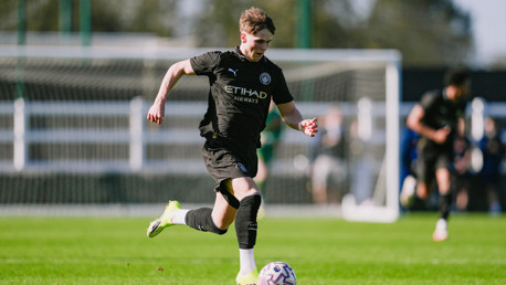 A soccer player in a Manchester City kit is running with the ball on a green field during a match.
