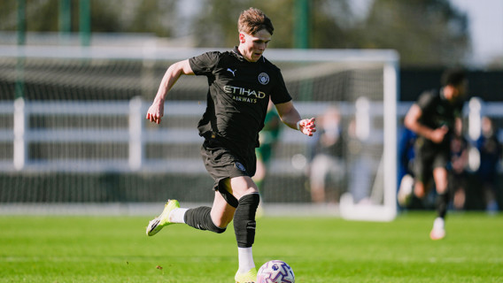 A soccer player in a Manchester City kit is running with the ball on a green field during a match.