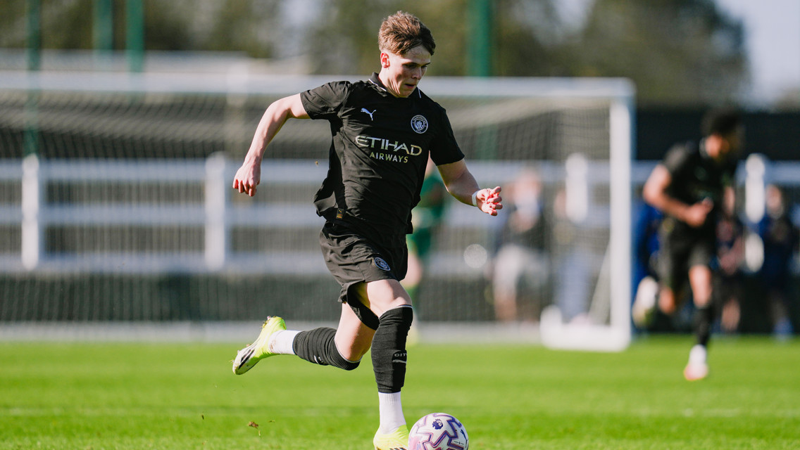 A soccer player in a Manchester City kit is running with the ball on a green field during a match.