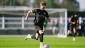 A soccer player in a Manchester City kit is running with the ball on a green field during a match.