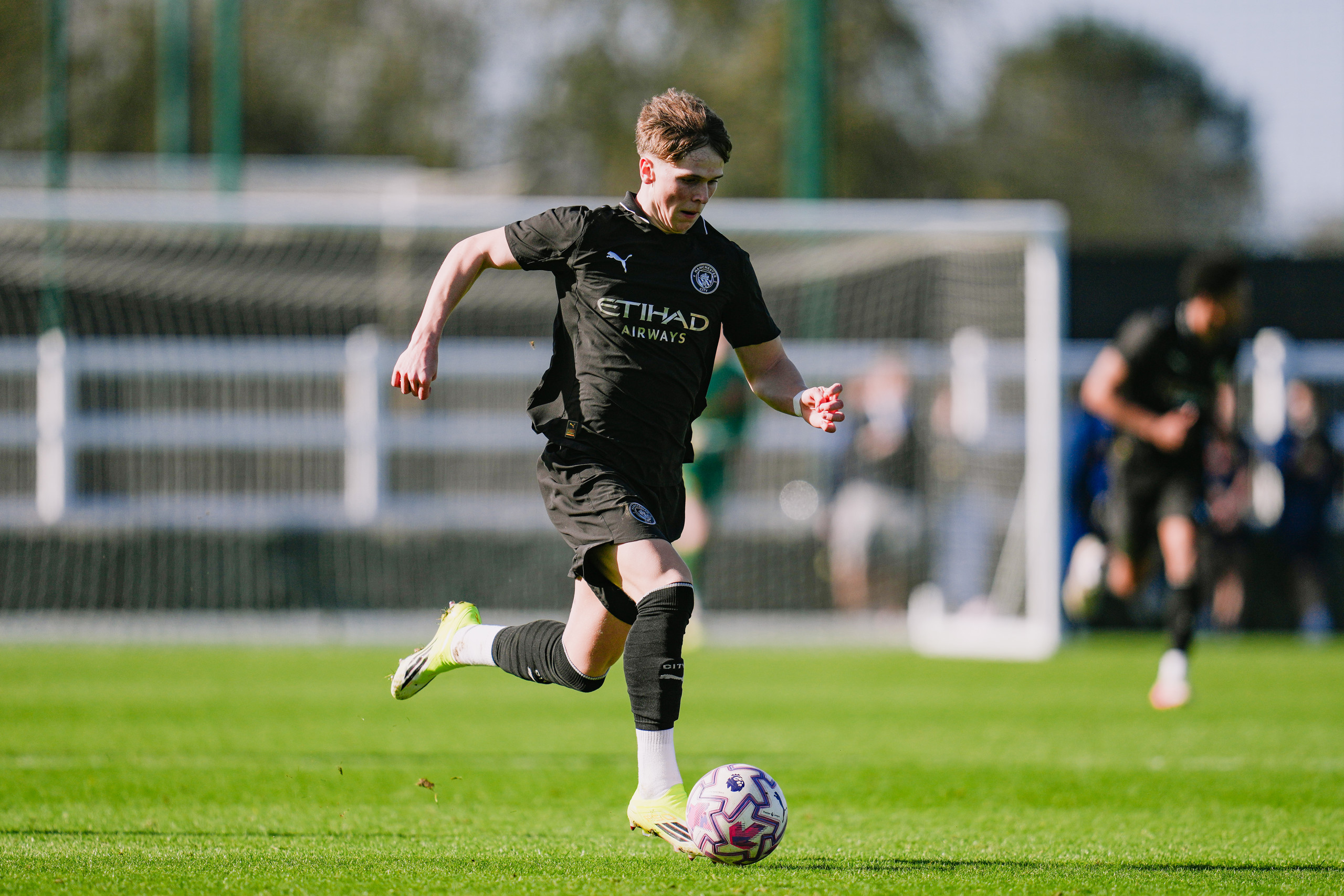 A soccer player in a Manchester City kit is running with the ball on a green field during a match.