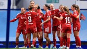 A group of Liverpool women's football team players in red kits are celebrating together on the field.