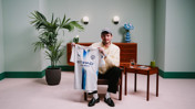 A person holding a Manchester City jersey with 'Etihad Airways' and Puma logos, sitting in a decorated room with plants and furniture.