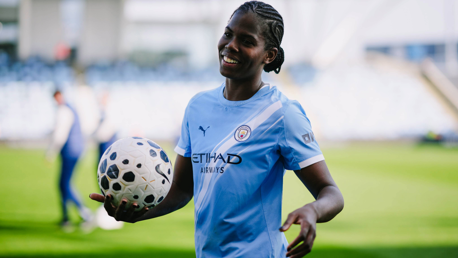 A football player in a Manchester City kit holding a ball on a soccer field.