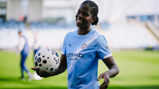 A football player in a Manchester City kit holding a ball on a soccer field.