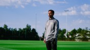 Individual in sports attire standing on a field with a clear sky. The attire has the New York City FC logo.