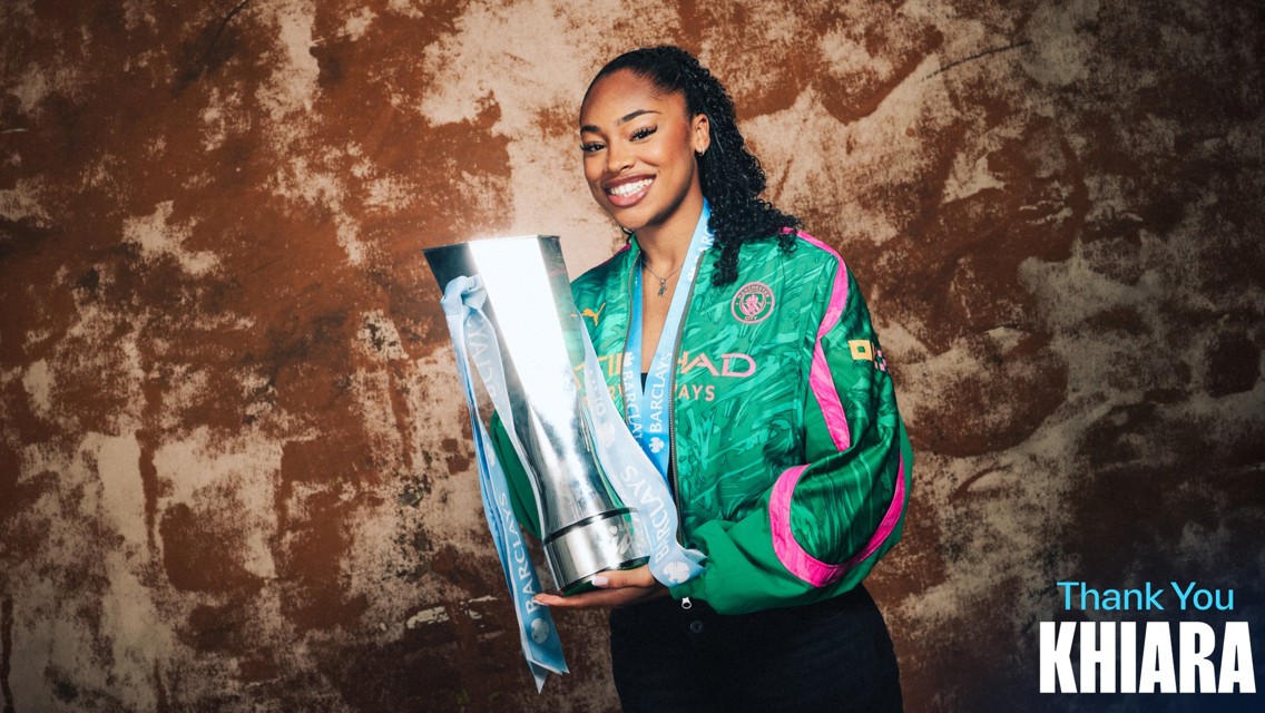 A person smiling while holding a large trophy, wearing a Manchester City jacket. The words 'Thank You Khiara' are seen on the image.