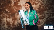 A person smiling while holding a large trophy, wearing a Manchester City jacket. The words 'Thank You Khiara' are seen on the image.