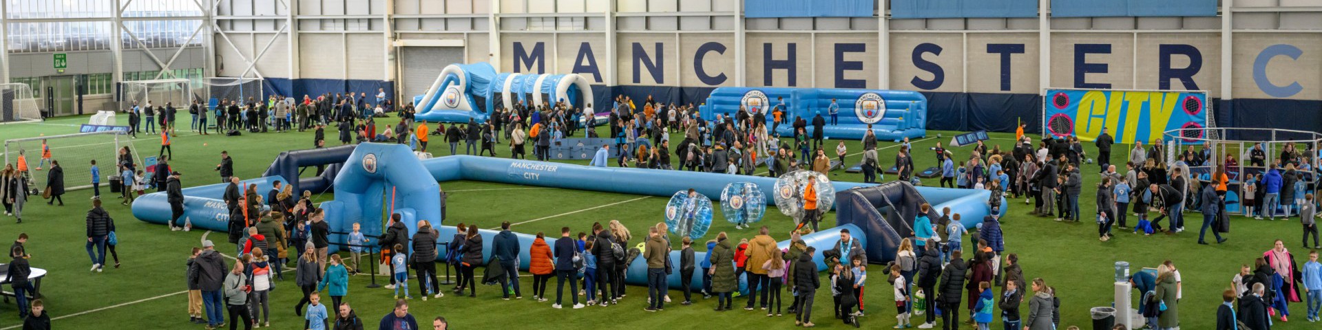 Indoor event at Manchester City's training facility with inflatable games and families enjoying activities.