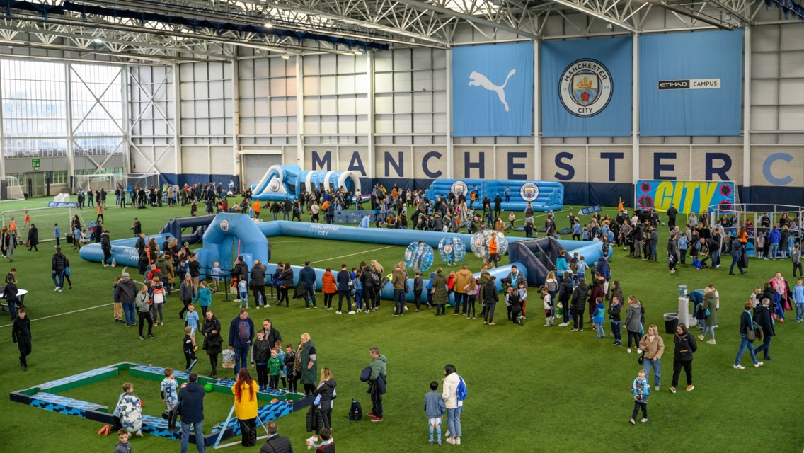 Indoor event at Manchester City's training facility with inflatable games and families enjoying activities.