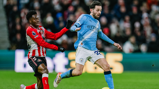 Two soccer players in action during a match. One wears a light blue Manchester City kit and the other a red and white Sunderland AFC kit.