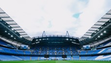 Panoramic view of an empty stadium with blue seats and large screens under a cloudy sky.