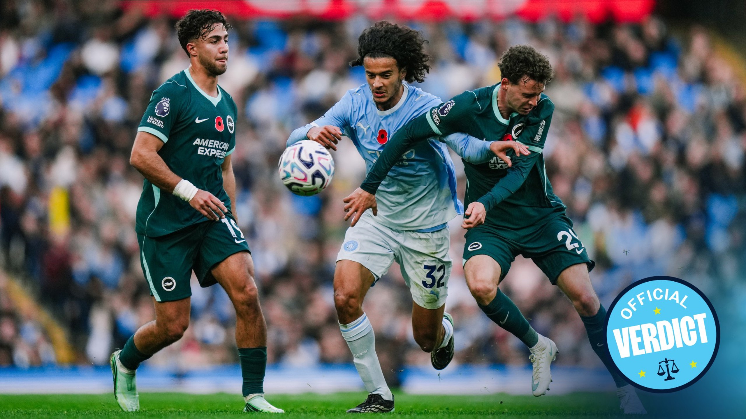 Three soccer players from different teams compete for the ball during a match. The player in blue is wearing a poppy badge on his shirt.